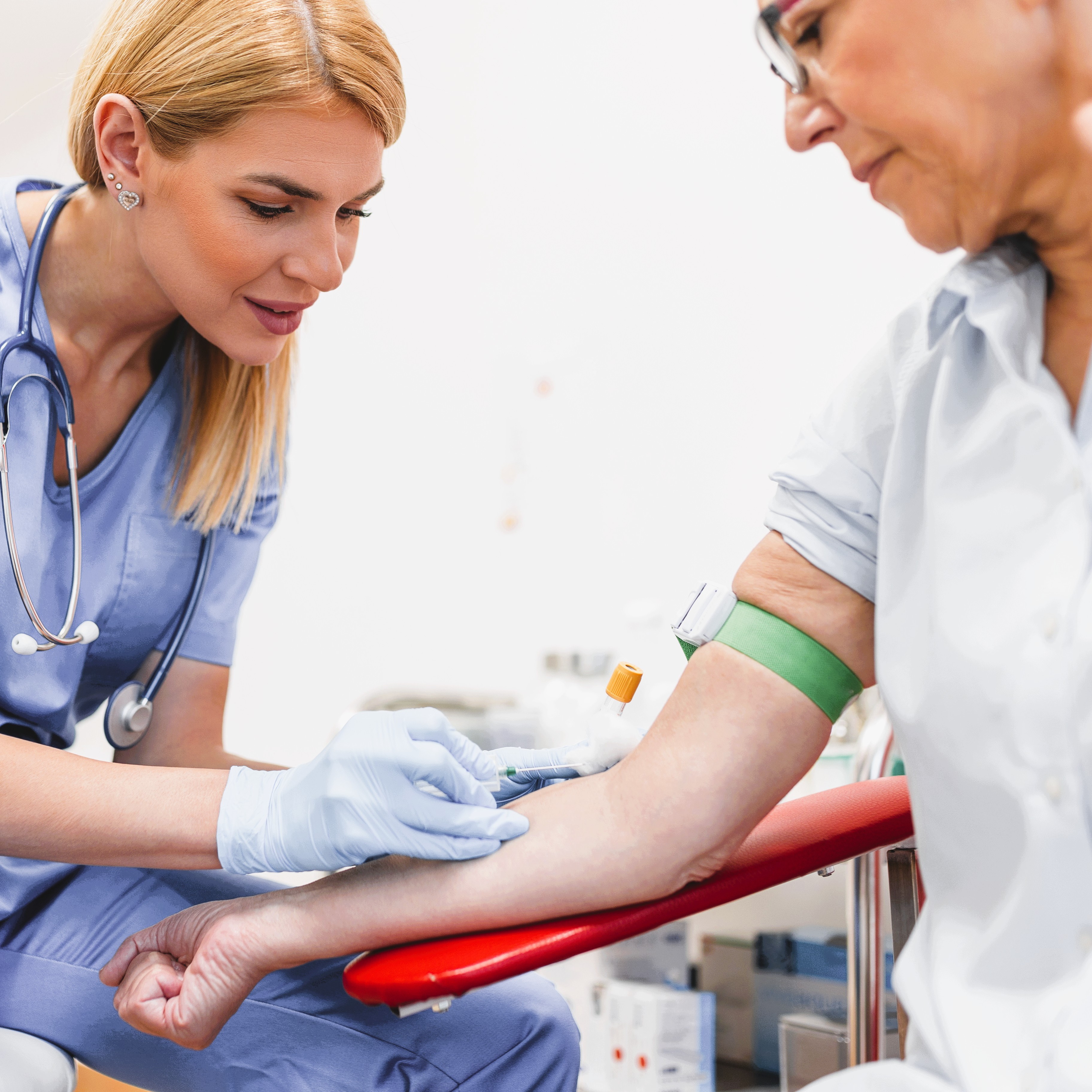 Eine medizinische Fachkraft bereitet sich darauf vor, einer sitzenden Patientin Blut abzunehmen.
