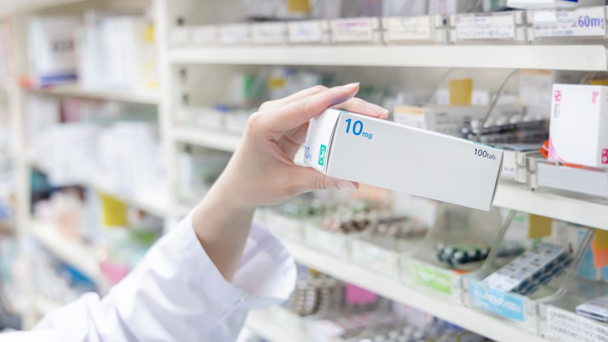 Die Hand eines Apothekers hält eine Medikamentenschachtel aus einem Apothekenregal